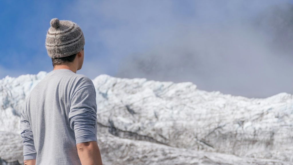 Man in a beanie gazing at the breathtaking snowy mountain landscape on a clear day.
